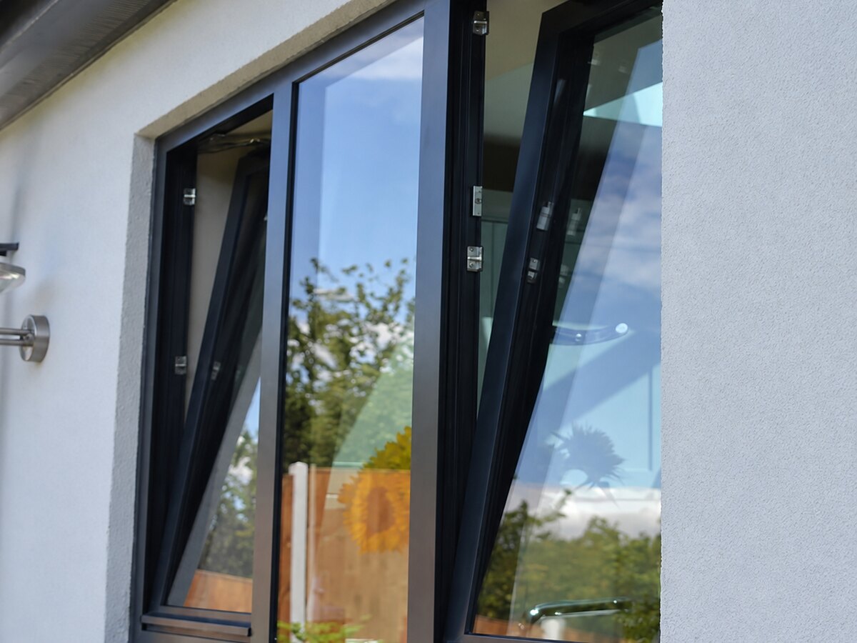 Black tilt-and-turn windows standing open on a rendered facade
